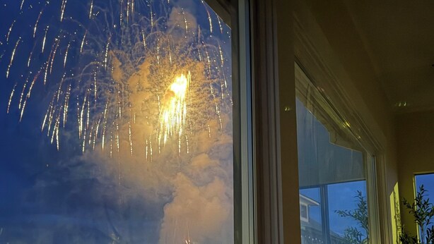 Une fenêtre donnant sur un spectacle de feux d’artifice dans le ciel nocturne.
