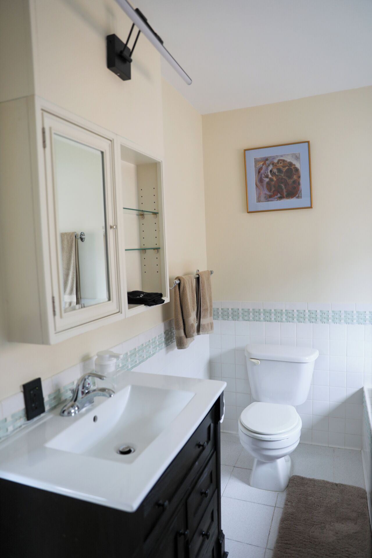 Un baño con un lavamanos blanco, un espejo, un inodoro y una obra de arte enmarcada en la pared.