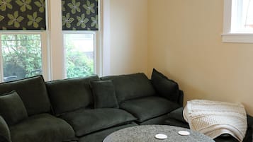 A living room with a sectional sofa, a round coffee table, and a window with a view of greenery.