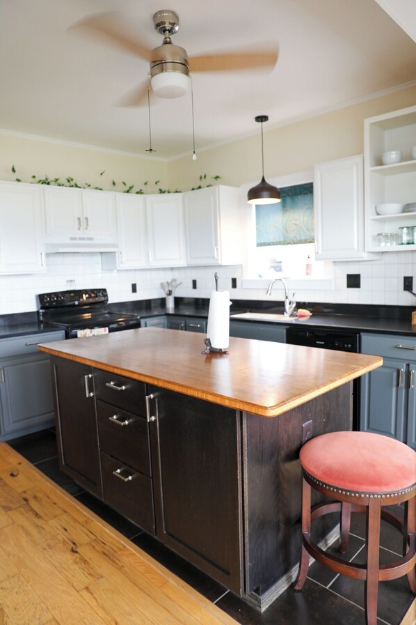 A kitchen with a central island, dark cabinetry, a wooden countertop, a hanging pendant light, and a bar stool.