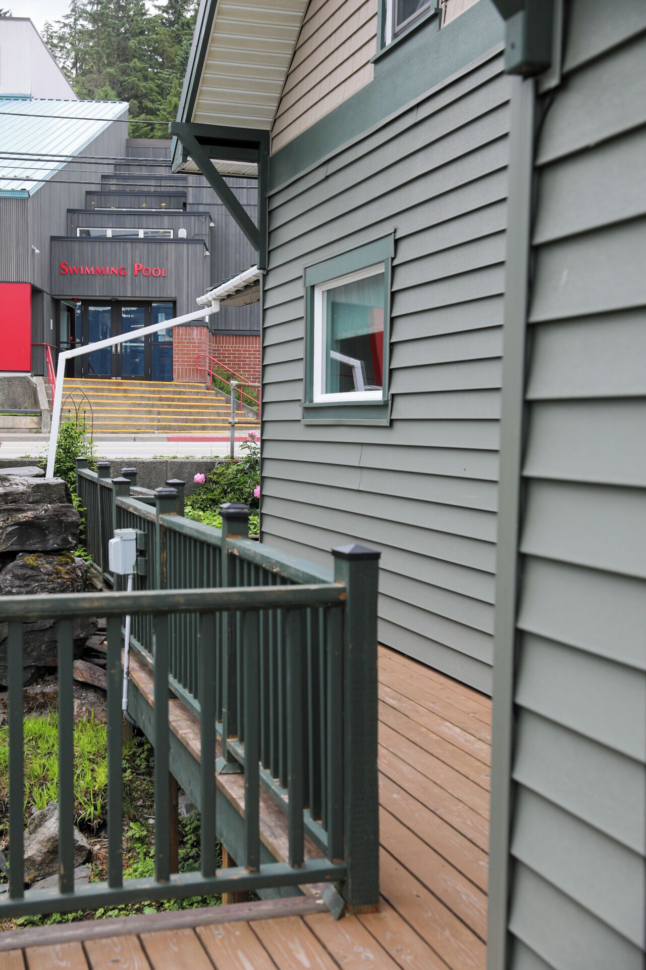A building with a swimming pool sign, a window, and a wooden deck with a railing.