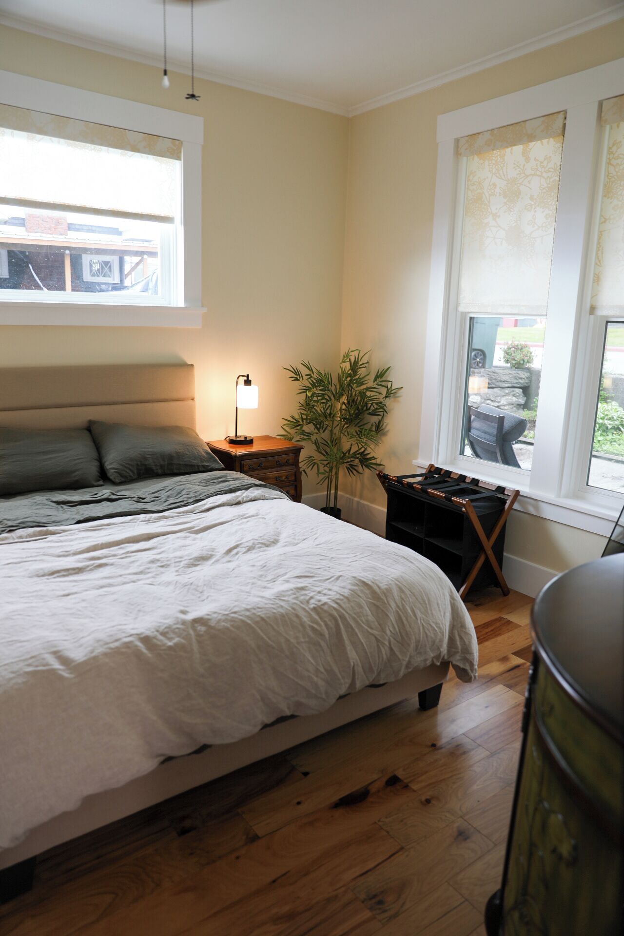 A bedroom with a large bed, bedside tables, a lamp, a potted plant, and a window with a view of the outside.