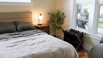 A bedroom with a large bed, bedside tables, a lamp, a potted plant, and a window with a view of the outside.