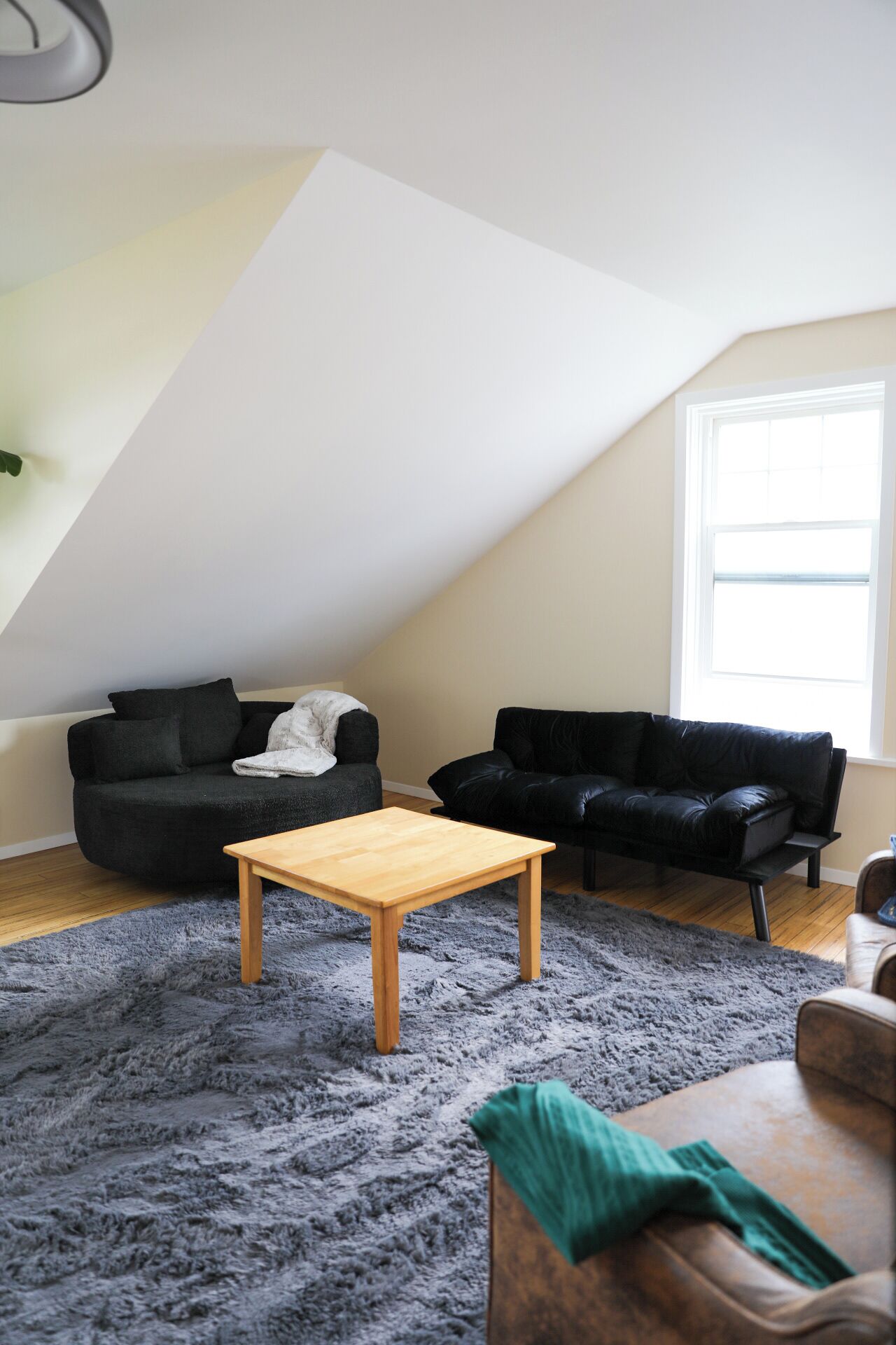 Ein Loft-Wohnzimmer mit hoher Decke, zwei schwarzen Ledersofas, einem Holztisch und einem grauen Shaggy-Teppich.