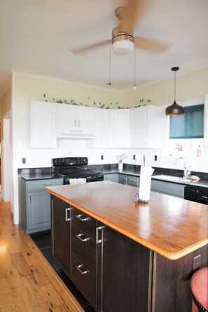 A kitchen with white cabinets, a wooden island with drawers, a black stove, and a ceiling fan.