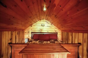 Un interno in legno con soffitto spiovente, un letto con testiera rossa e una piccola finestra.