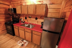 Eine kleine Küche mit Holzwänden, einem Edelstahlkühlschrank, einer Mikrowelle und einem Herd.