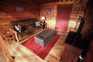 Ein Interieur einer Hütte mit Holzboden, einer Couch, einem roten Teppich, einem Fernseher und einer roten Tür.