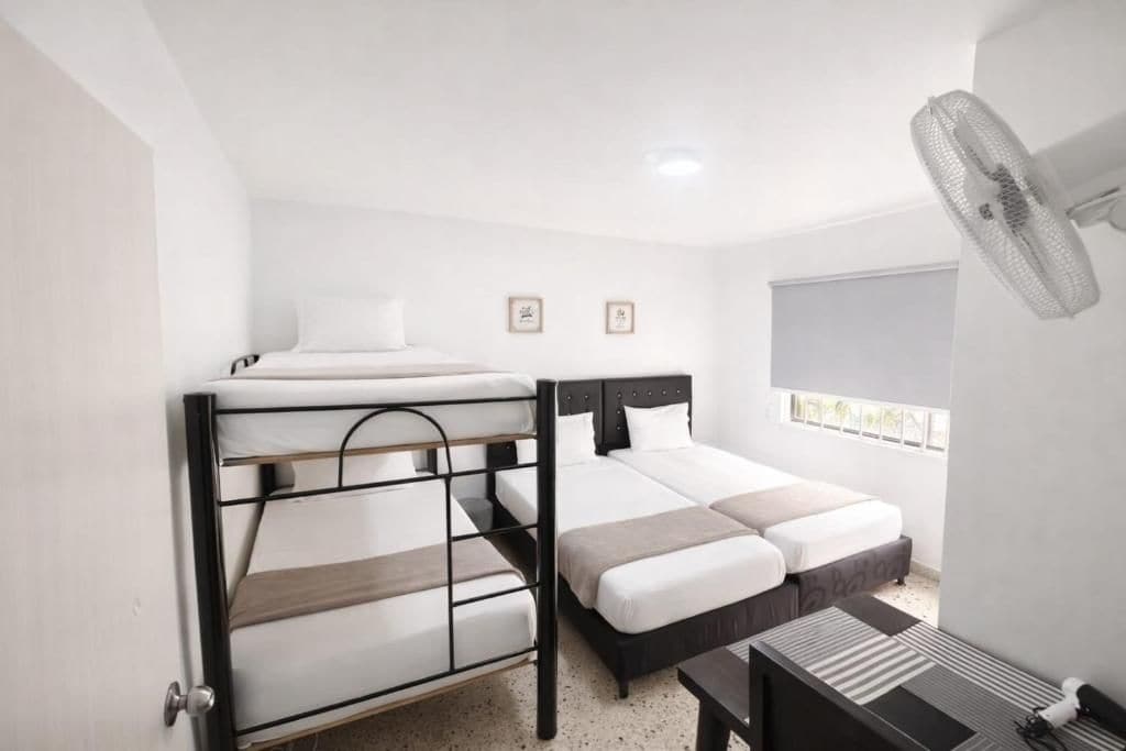 Une chambre avec des lits superposés, un bureau, une chaise, un ventilateur et une fenêtre avec des stores.