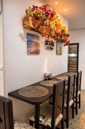 Un'area pranzo con un tavolo lungo, sedie e un muro decorato con un'asse floreale e quadri incorniciati.