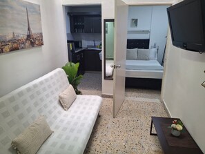Un ambiente compatto con angolo cottura, un letto, una TV e un tavolino con un vaso.