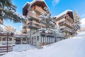 A multi-story building with balconies, stone facade, and snow-covered surroundings. - Mountain atmosphere at the ski lift departure area (Sauze d'Oulx)