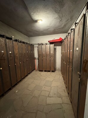 A locker room with numbered lockers, a red storage unit, and a pair of skis leaning against the wall. - Mountain atmosphere at the ski lift departure area (Sauze d'Oulx)