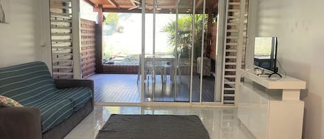 A living room with a sofa, a television on a stand, and a sliding glass door leading to an outdoor area.