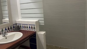 Ein Badezimmer mit einem weißen Waschbecken, einem Spiegel und einem Fenster mit horizontalen Rollläden.