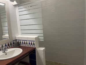 Een badkamer met een wit wastafelmeubel, een spiegel en een raam met horizontale jaloezieën.