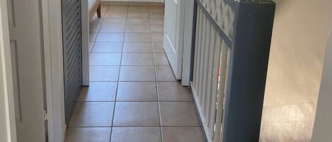 Un couloir au sol carrelé, une fenêtre donnant sur un espace verdoyant et une porte menant à un balcon.