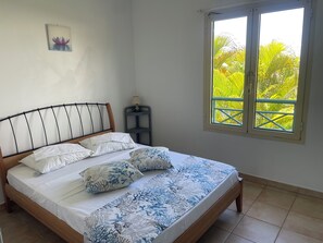 Een bed met een houten hoofdbord, wit beddengoed en blauwe kussens met een bloemendessin. Een tafeltje met een lamp staat ernaast.