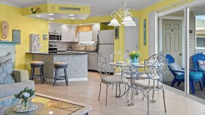 Una cuina moderna amb armaris blancs, una zona de menjador amb cadires metàl·liques i una paret d'accent de color groc brillant.