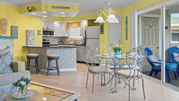 Een moderne keuken met witte kasten, een eetgedeelte met metalen stoelen, en een felgele accentmuur.