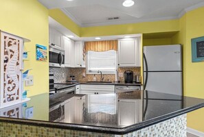 A kitchen with white cabinets, a black countertop, and a white refrigerator. - North Myrtle Beach Cherry Grove Getaway Beautiful Views Peaceful Coastal Retreat (North Myrtle Beach)