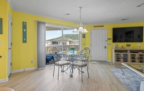 Un coin repas avec une table ronde et des chaises, un lustre et une vue sur un bâtiment, visible à travers une porte-fenêtre coulissante.