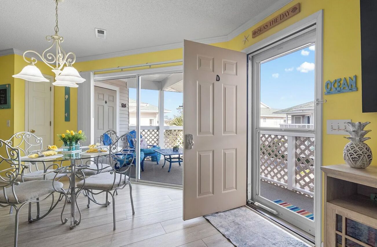 A dining area with a table and chairs, a chandelier, and a view through a door to the outside.