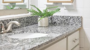 Ein Badezimmer mit einer Arbeitsplatte aus Granit, einem Waschbecken, einem Spiegel und zwei gerahmten Bildern an der Wand.