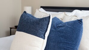 Ein Bett mit weißen und blauen Kissen, ein gerahmtes Bild an der Wand und ein Nachttisch mit einer Lampe.