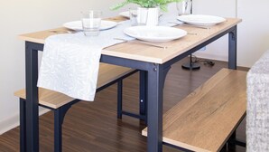 Ein Essbereich mit einem Holztisch, gedeckt für zwei Personen, einer Topfpflanze und einem gerahmten Zitat an der Wand.