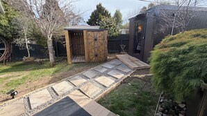 A backyard with a wooden shed, a metal gate, a paved walkway, and a small garden area. - SQ Property; Autumn Hideaway. Customisable layout for small or large groups (Palmerston North)