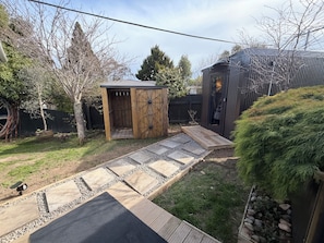 Un patio trasero con un cobertizo de madera, una reja metálica, un sendero pavimentado y una pequeña zona de jardín.