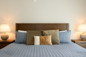 A bed with a wooden headboard, multiple pillows, and two bedside lamps on wooden nightstands.