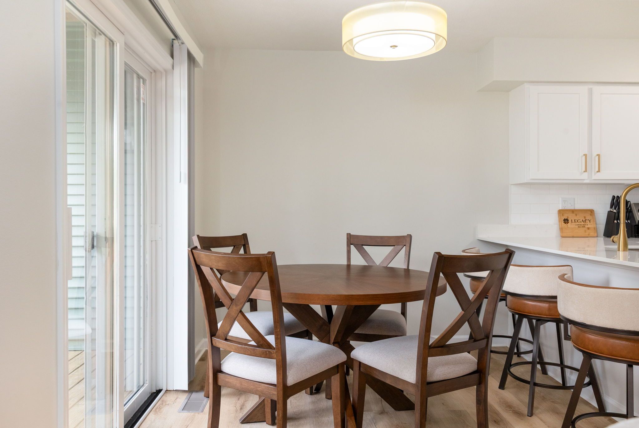 Un coin repas avec une table ronde et quatre chaises, une cuisine avec des meubles blancs et un luminaire au plafond.