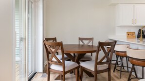 A dining area with a round table and four chairs, a kitchen with white cabinets, and a ceiling light fixture.