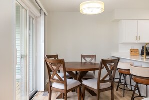 Un comedor con una mesa redonda y cuatro sillas, una cocina con armarios blancos y una lámpara en el techo.