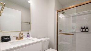 A modern bathroom with a white sink, gold faucets, a glass shower enclosure, and a toilet.