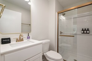 Un baño moderno con un lavamanos blanco, grifos dorados, una cabina de ducha de vidrio y un inodoro.
