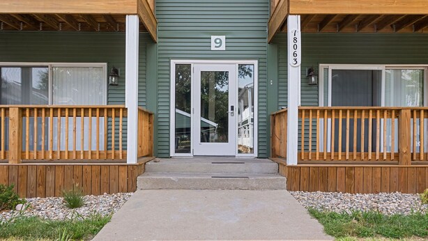 A two-story building with a green exterior, numbered 9, and a wooden porch with a concrete pathway leading to the entrance.