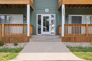 A two-story building with a green exterior, numbered 9, and a wooden porch with a concrete pathway leading to the entrance.