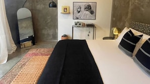 A bedroom with a bed, a bedside table, a mirror, a wall-mounted shelf with items, and a framed picture. - Bohemio Raconteur: Four Suites + Sauna + Pickleball + Walkable Marfa (Marfa)