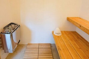 A sauna room with a wooden bench, a metal heater, and a white bottle labeled 'BOHEMIO'.