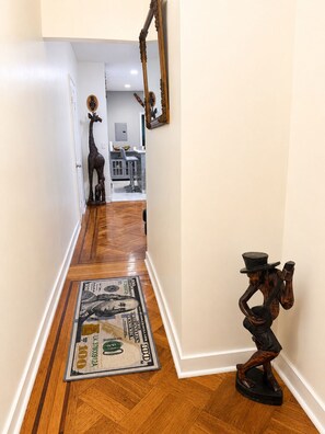 A hallway with a wooden floor, a dollar bill rug, and a giraffe sculpture. - Spacious Stay Near EWR, Parks & Transit (Newark)