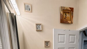 Un baño con un lavabo blanco, un espejo y una puerta. Hay interruptores de luz en la pared y una pequeña botella de jabón.