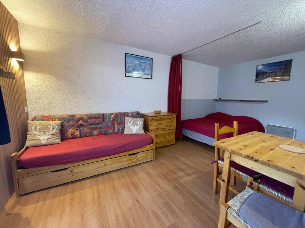 A compact room with a wooden sofa, a small wooden table, a red bed, and a wooden dresser.