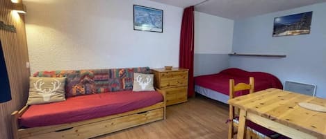 A compact room with a wooden sofa, a small wooden table, a red bed, and a wooden dresser.