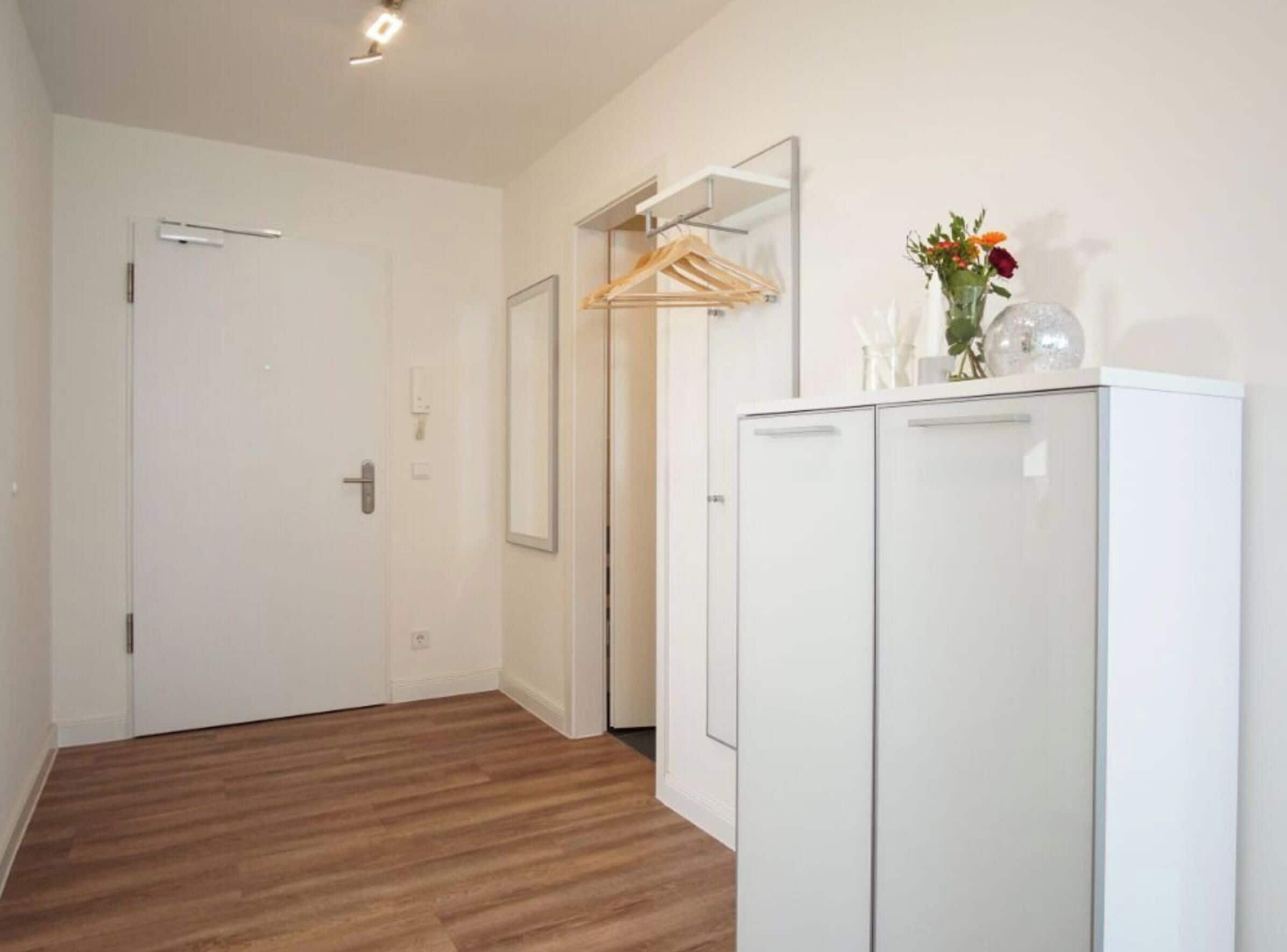 A hallway with a wooden floor, a white wardrobe, a door, and a wall-mounted drying rack.