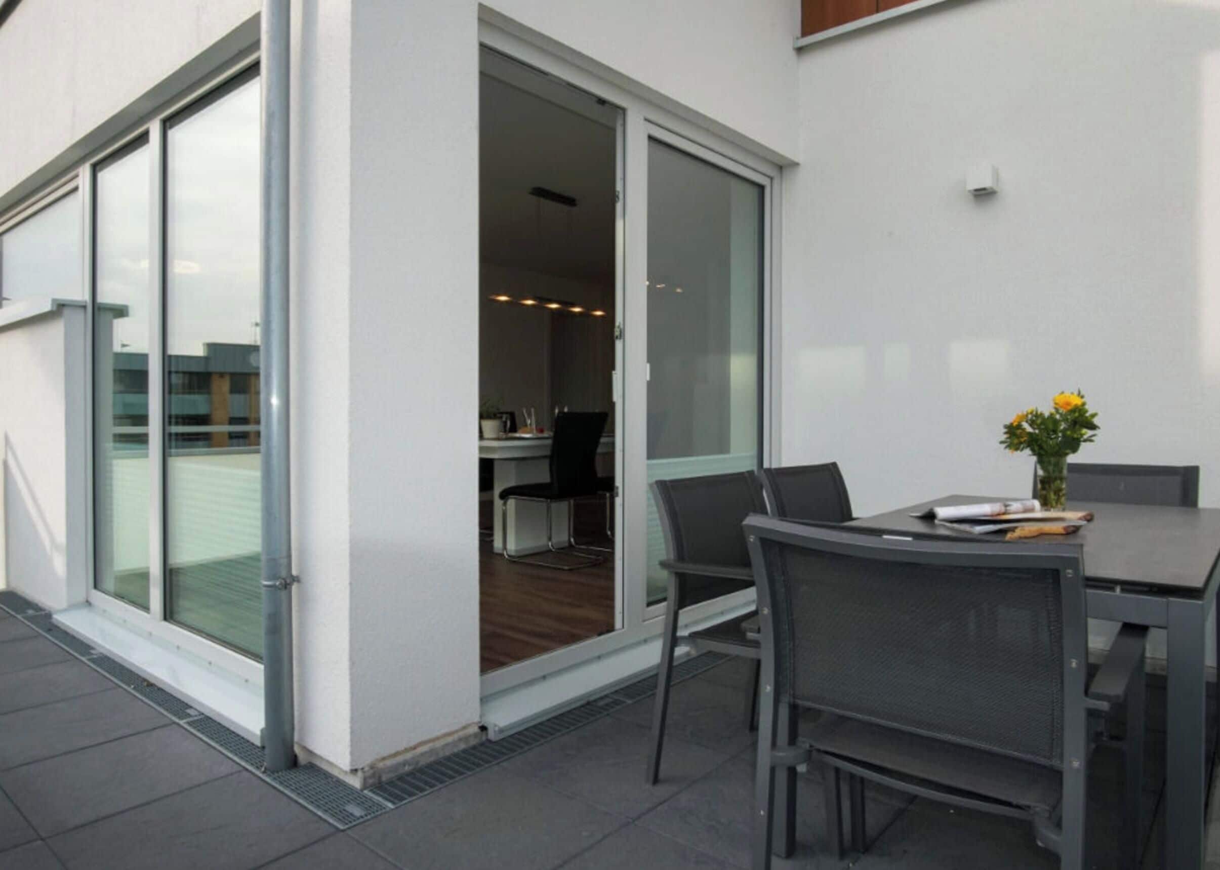 An outdoor patio with a table and chairs, a sliding glass door leading to an interior space, and a small plant on the table.