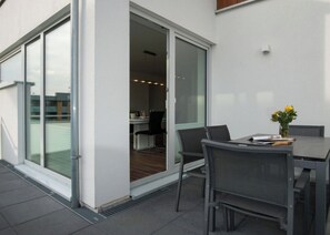 Eine Außenpatio mit Tisch und Stühlen, eine Glastür, die in einen Innenbereich führt, und eine kleine Pflanze auf dem Tisch.