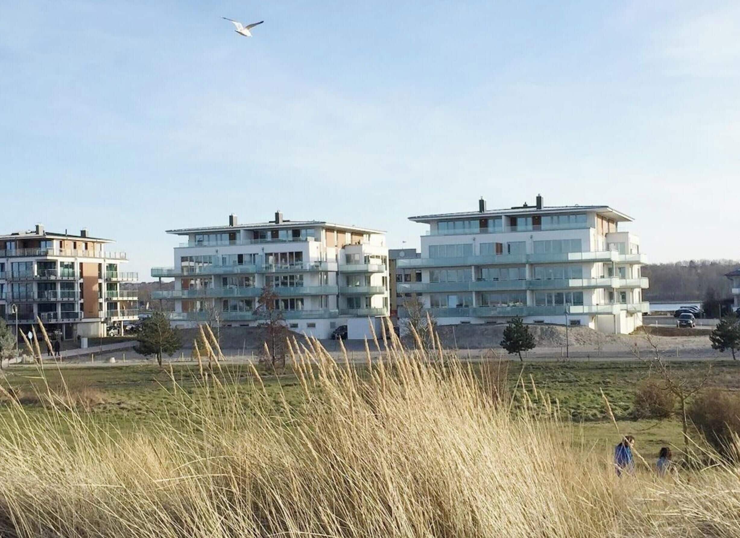 A modern residential building with multiple floors and balconies, surrounded by open grassy areas and a clear sky.